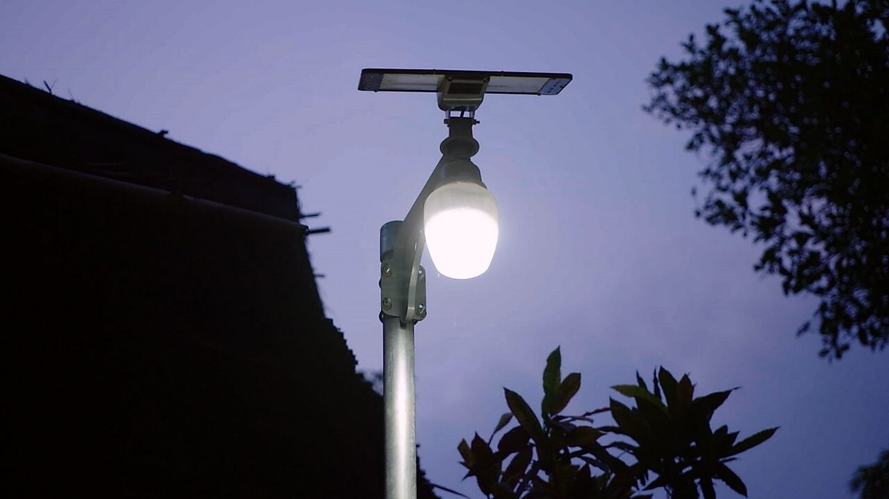 Imagem de uma lâmpada acesa em um poste de luz, com uma placa solar acima.