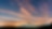 Imagem distante de um monte com turbinas eólicas lado a lado, ao entardecer. Vemos um céu azul escuro e nuvens alaranjadas.