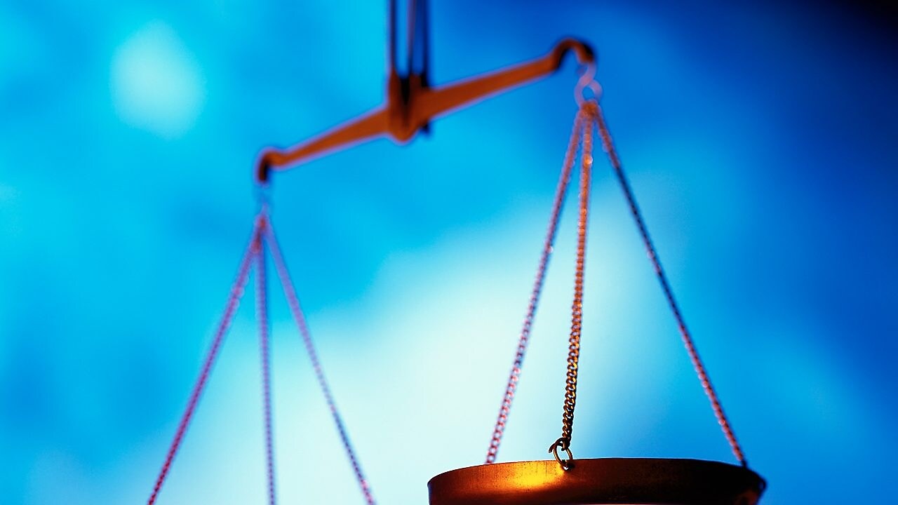 Imagem de uma balança de dois pratos dourada, com fundo azul.