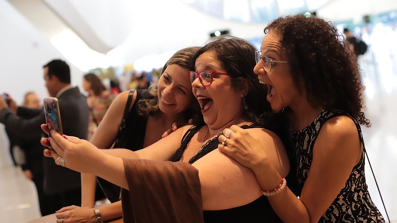 Na foto, vemos três mulheres animadas e sorridentes, enquanto posam por um selfie.