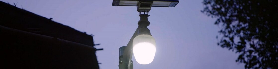 Imagem de uma lâmpada acesa em um poste de luz, com uma placa solar acima.