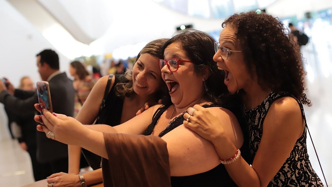 Na foto, vemos três mulheres animadas e sorridentes, enquanto posam por um selfie.