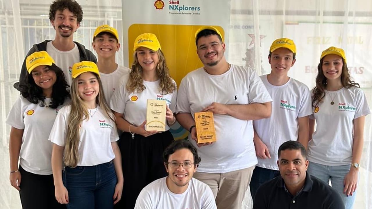 Um grupo de jovens sorrindo em fundo neutro, segurando uma placa de madeira