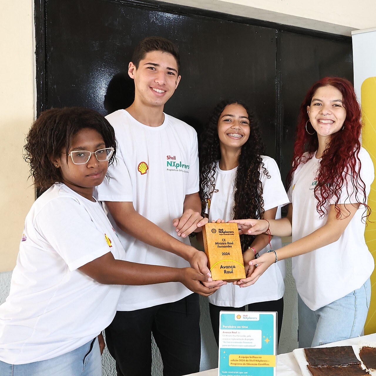 Quatro jovens segurando uma placa de madeira em um fundo neutro