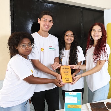 Quatro jovens segurando uma placa de madeira em um fundo neutro